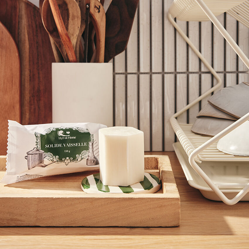 Savon solide pour la vaisselle emballé dans un sachet blanc avec une étiquette verte, illustré avec des ustensiles de cuisine et le texte 'Savon Vaisselle Dish Soap Bar"