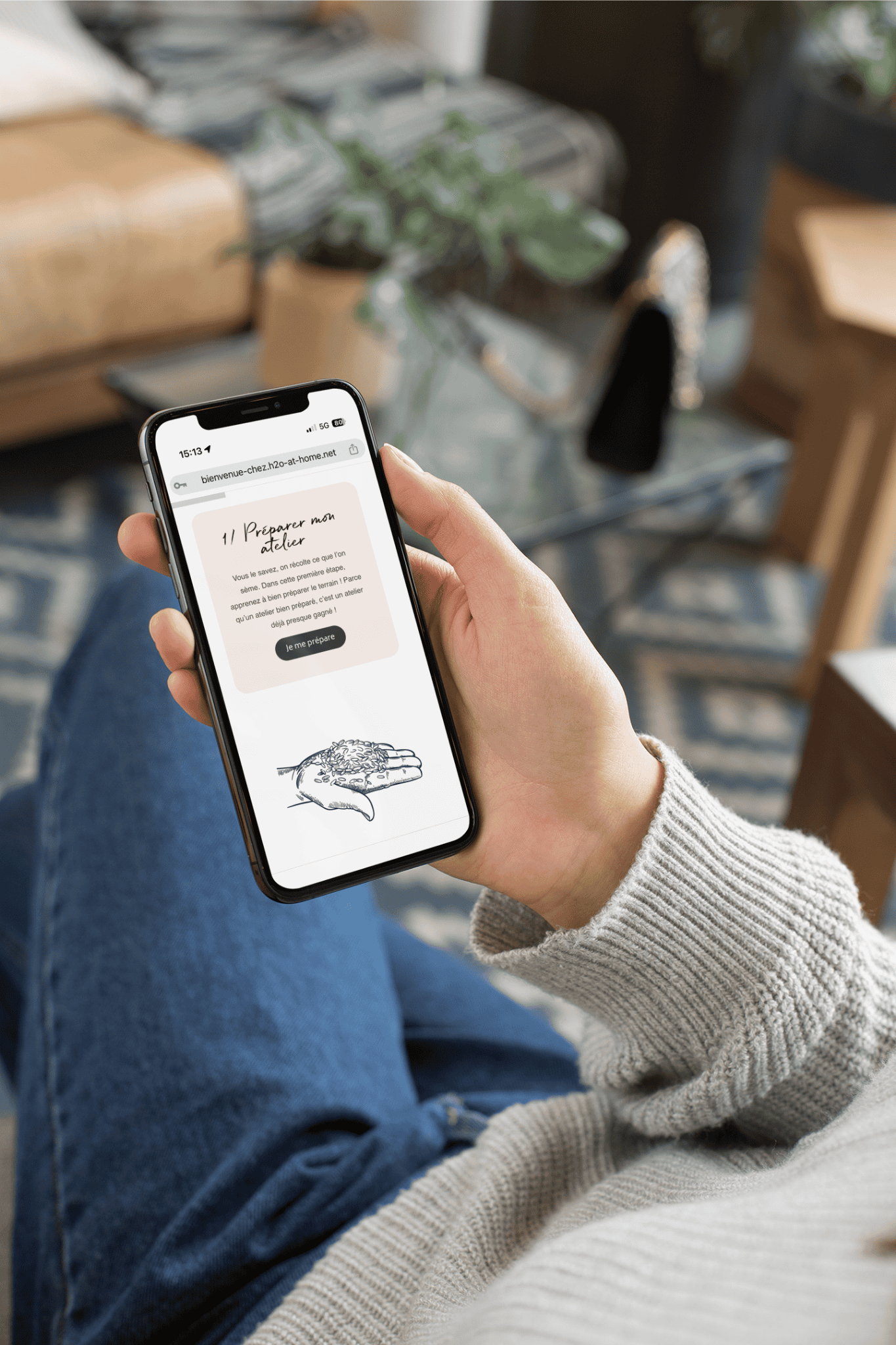 Personne tenant un smartphone affichant une page web d'un atelier créatif avec un dessin de main et une zone d'instructions intitulée 'Préparer mon atelier
